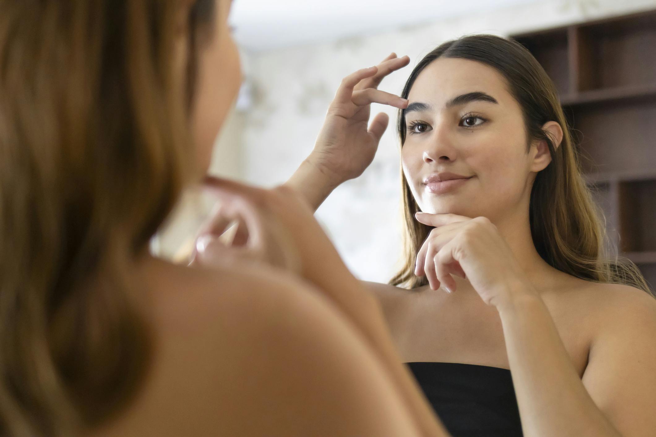 woman examining her brows in the mirror
