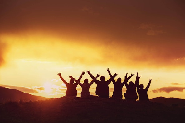 Group of six people, cheering at sunset on a mountain