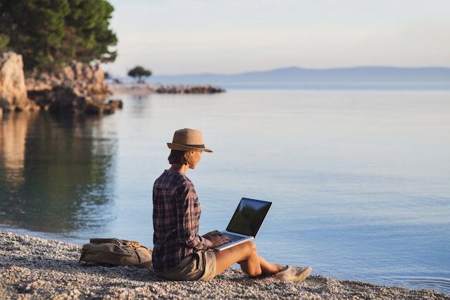 Vrouw die haar computer op een strand gebruikt