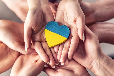 A group of hands holding a wooden heart painted with the Ukrainian flag