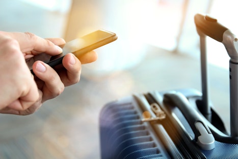 A phone is a persons hands in front of a suitcase