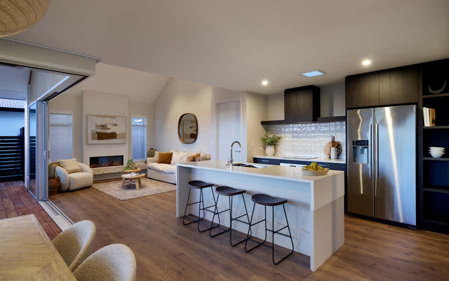 Contemporary kitchen and lounge by Signature Homes featuring dark cabinetry, stone island, stainless steel fridge, and open-plan living with high ceilings