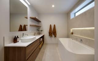 Contemporary bathroom design by Signature Homes featuring a deep bathtub, timber vanity with vessel basin, wall shelving, and tiled feature wall with LED lighting