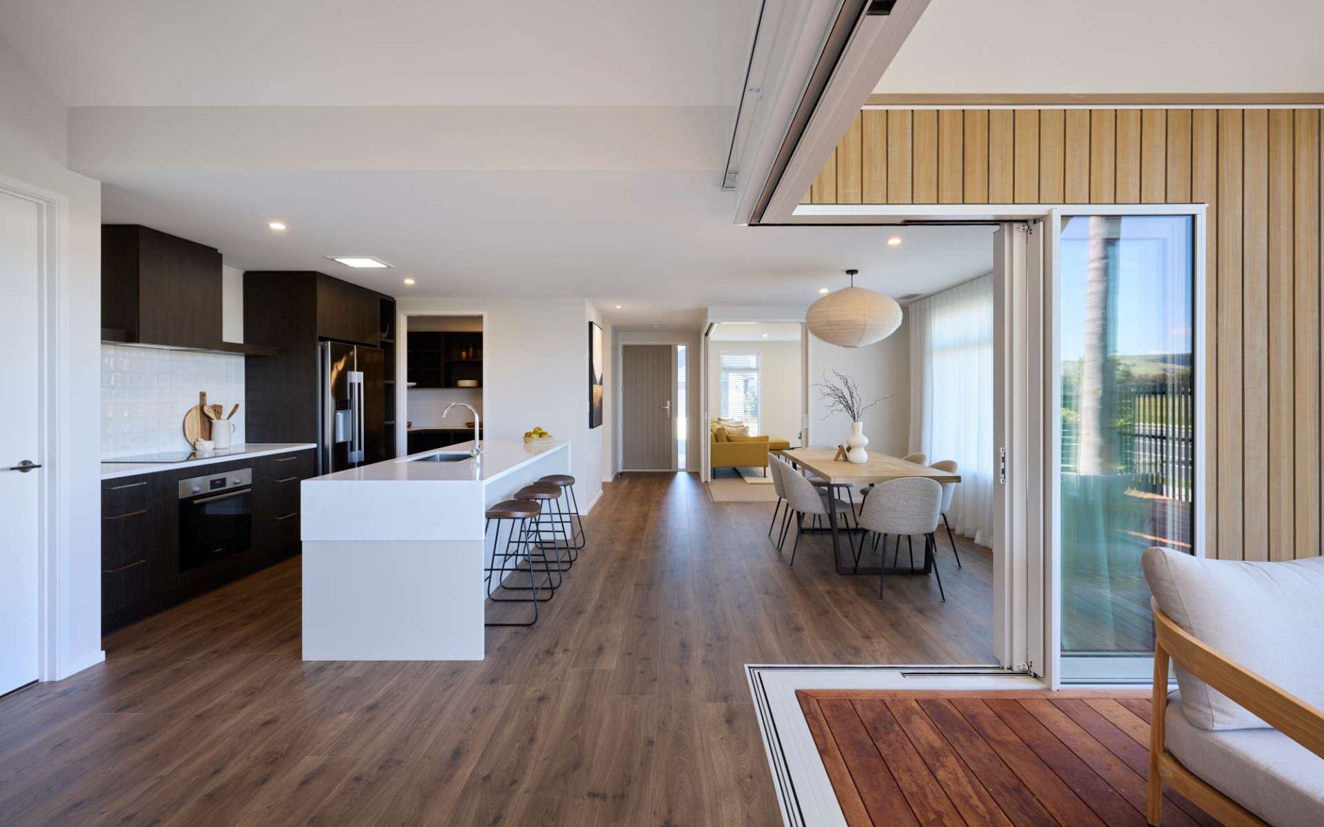 Contemporary kitchen and dining area with dark wood cabinetry, stone island bench, and sliding glass doors opening to a sunlit deck