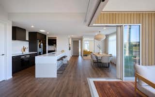 Contemporary kitchen and dining area with dark wood cabinetry, stone island bench, and sliding glass doors opening to a sunlit deck