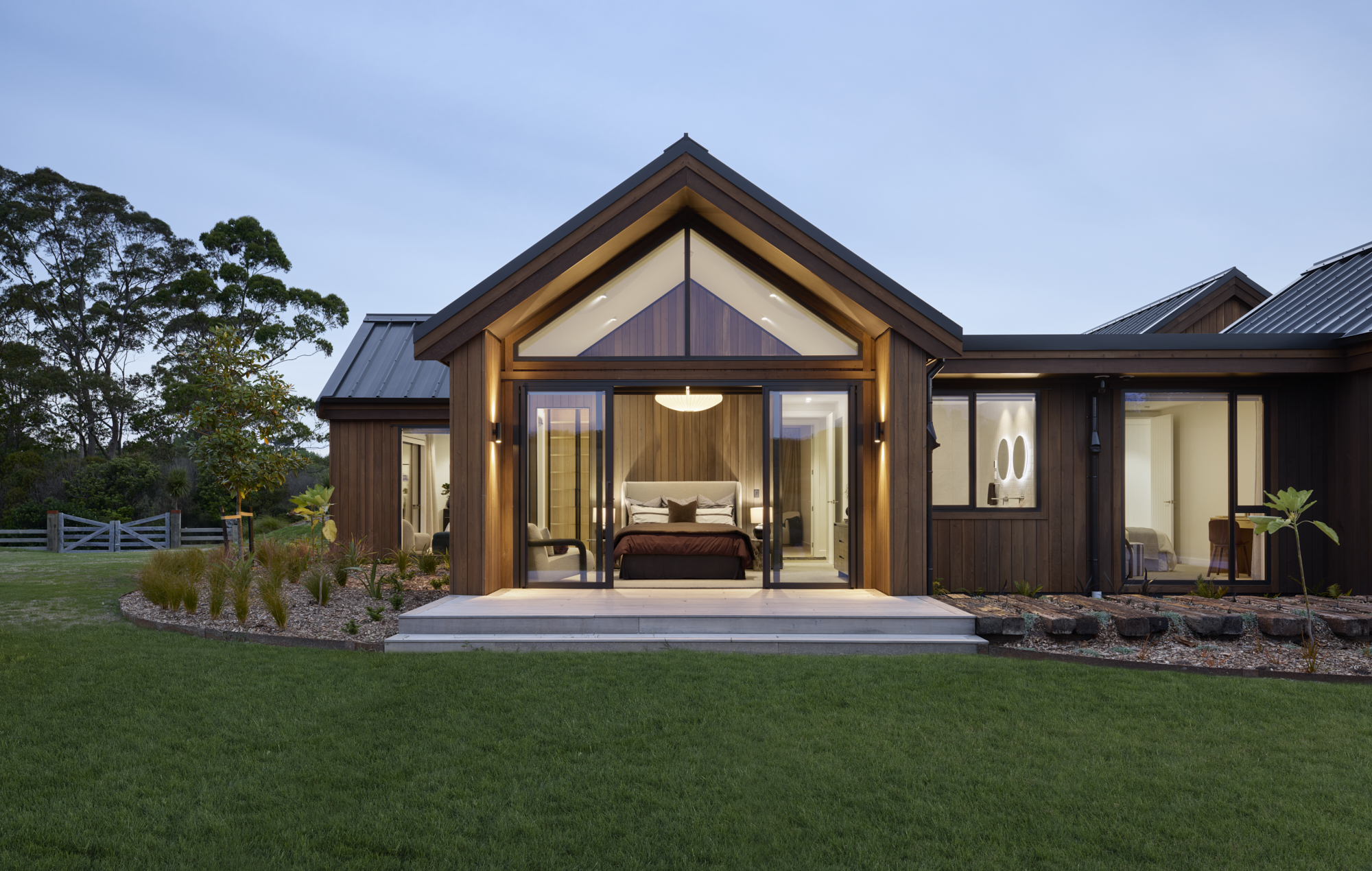 Master bedroom with gable ceiling, floor-to-ceiling windows, and cedar feature wall opening to landscaped gardens.