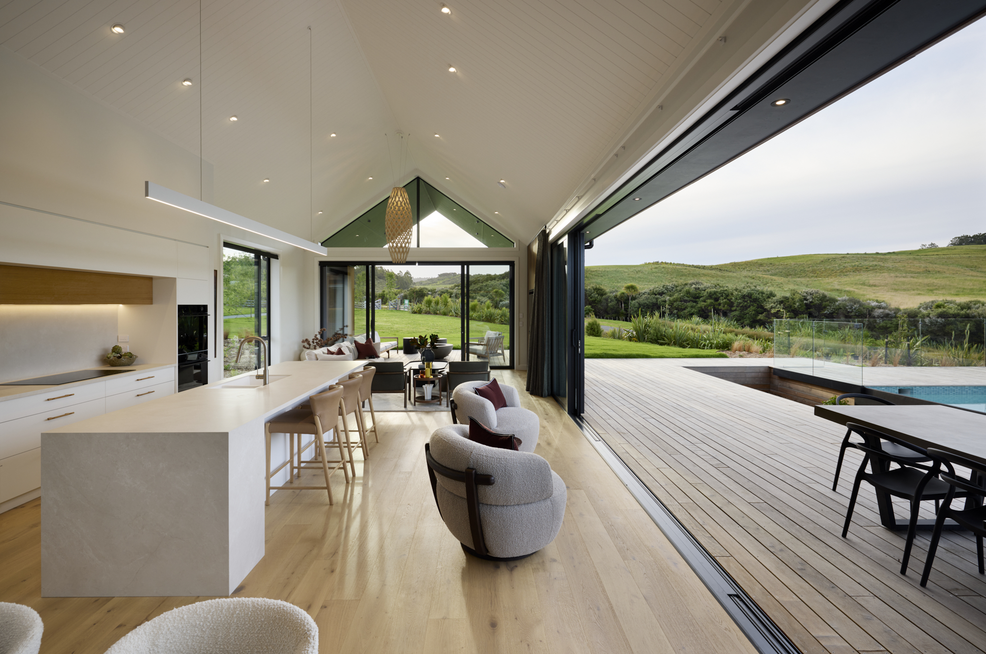 Open-plan kitchen and living area with vaulted ceiling and seamless indoor–outdoor flow to pool and decking.