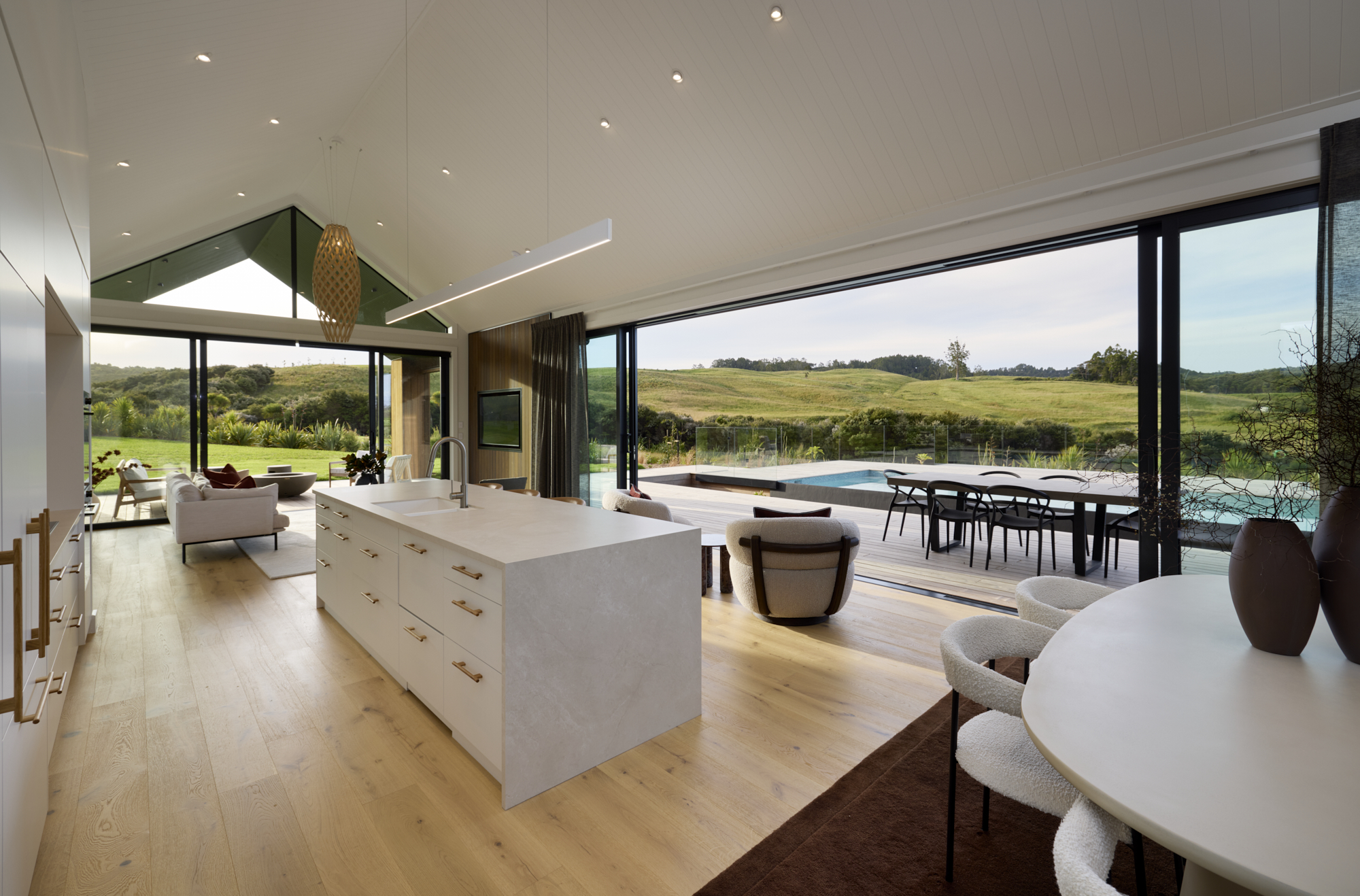 Contemporary kitchen and dining area overlooking outdoor pool and countryside through large sliding glass doors.