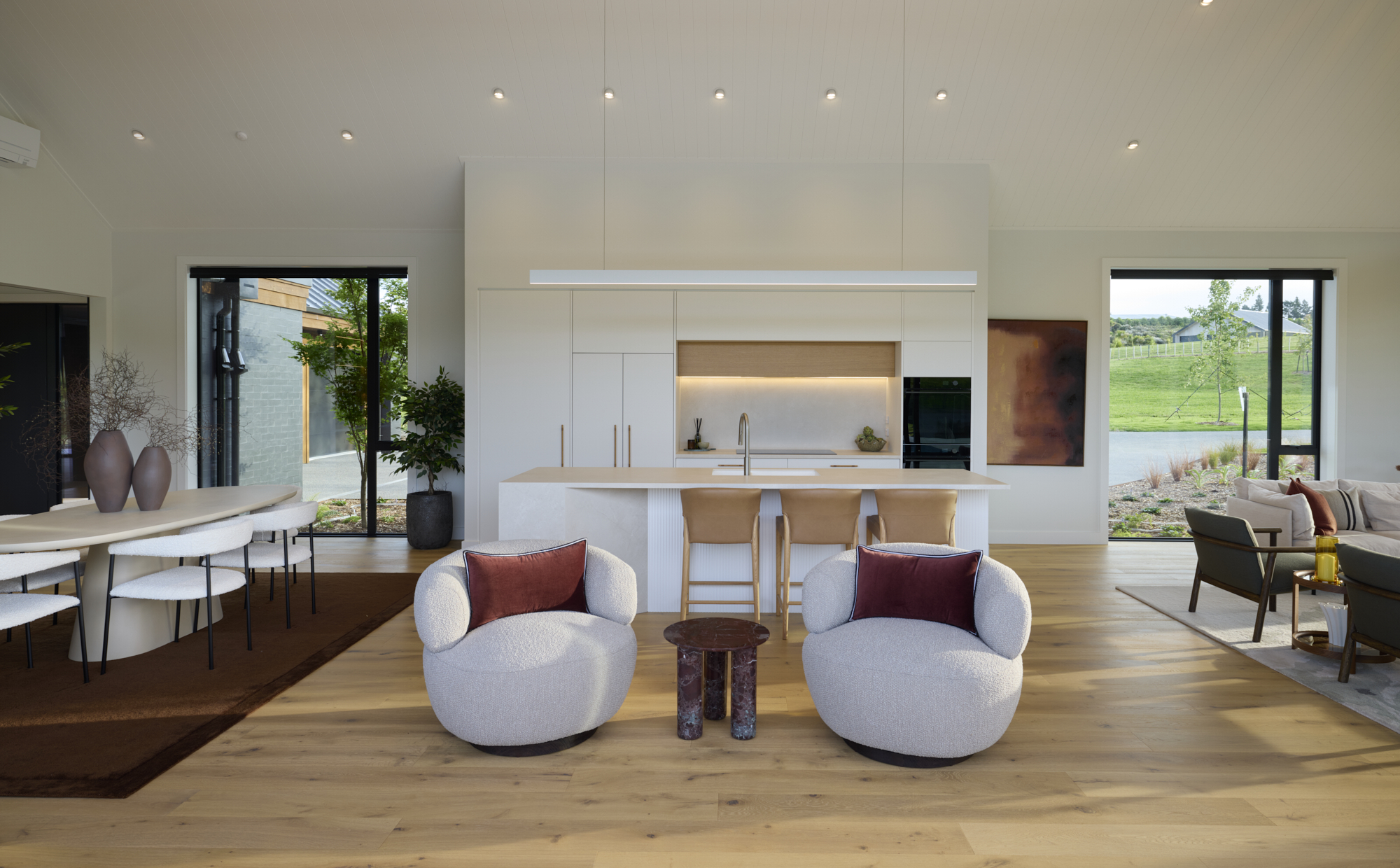 Modern living space featuring a minimalist kitchen island, lounge chairs, and panoramic rural views.