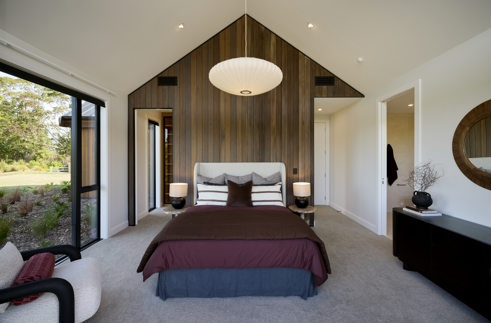 Stylish master bedroom with cedar feature wall, neutral bedding, and large windows bringing in natural light.