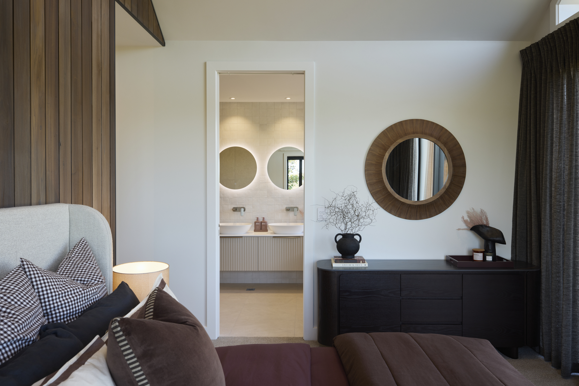 Ensuite bathroom view from master bedroom showcasing double vanities, round mirrors, and modern design details.
