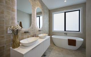Modern bathroom with double vessel basins, curved backlit mirrors, freestanding bathtub and warm neutral tiles
