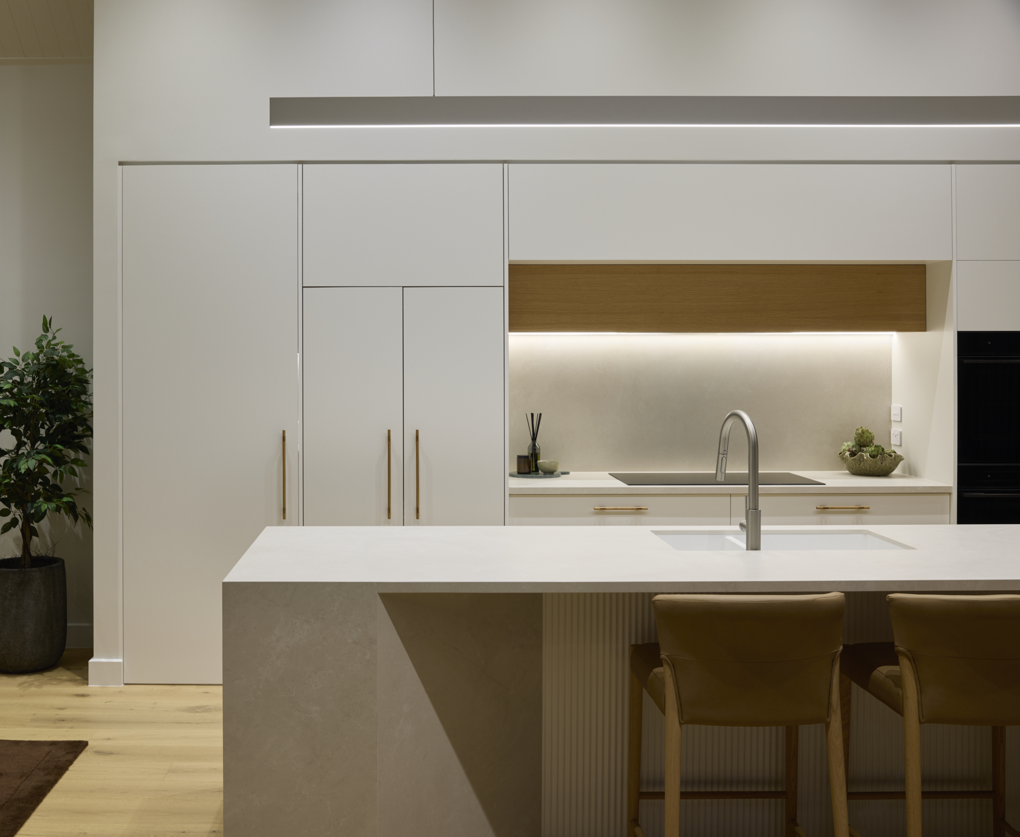Minimalist kitchen with integrated cabinetry, stone island bench, warm timber accents, and soft under-cabinet lighting.