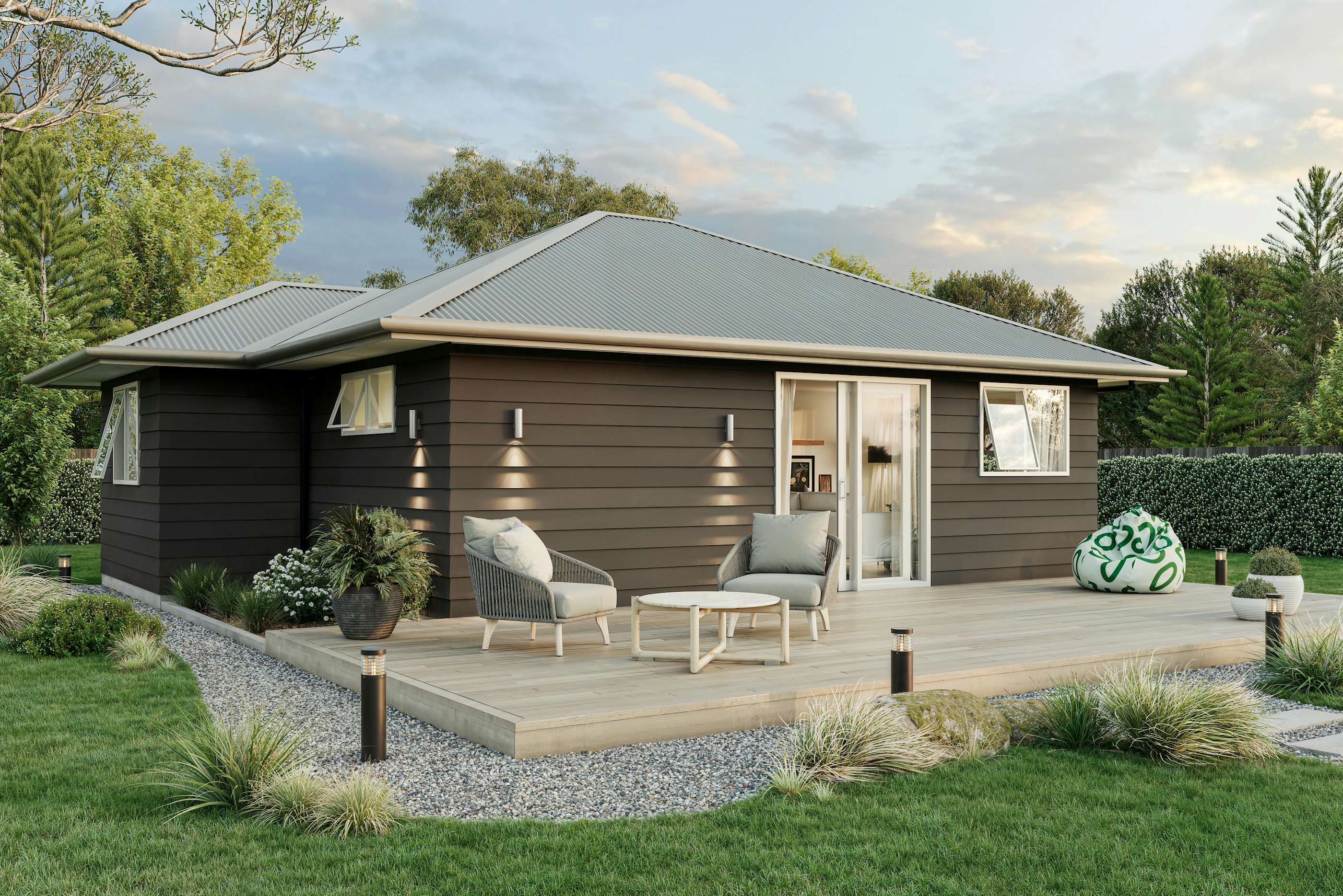 Two-bedroom minor dwelling exterior with timber deck, dark weatherboard cladding, and outdoor seating, designed by Signature Homes.