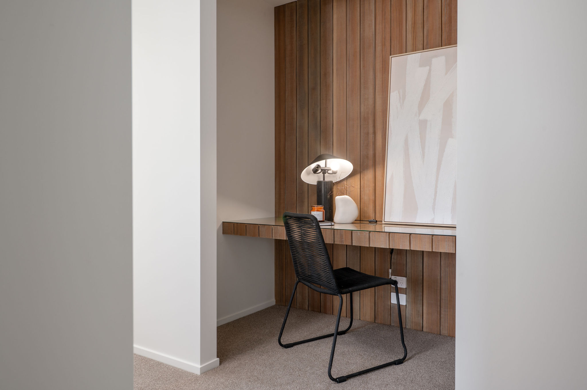 Built-in timber-panelled study nook with floating white desk, black rope chair, modern mushroom table lamp, and abstract wall art