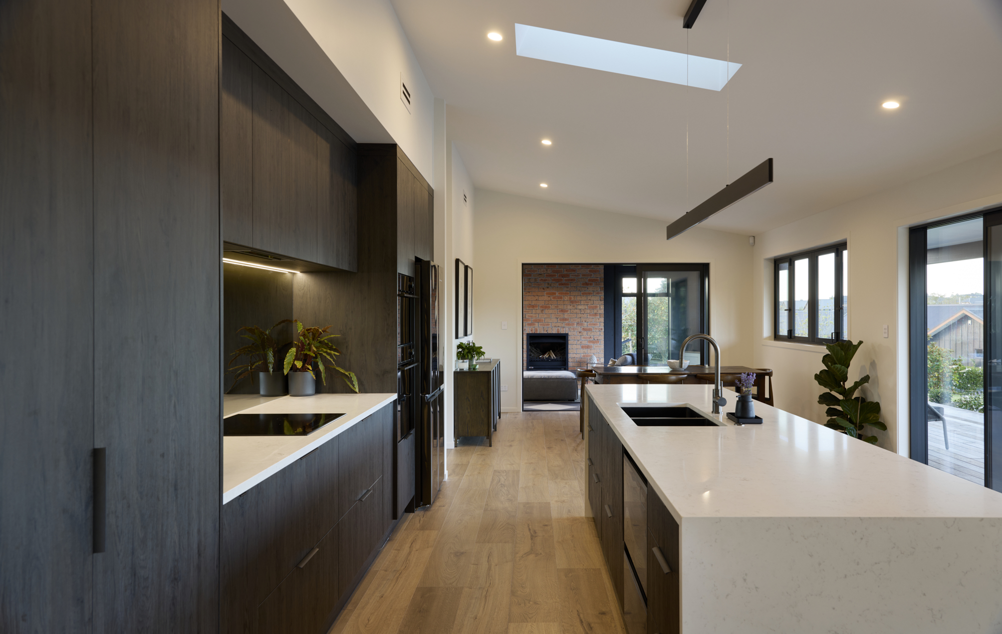 Interior view from the kitchen island looking through a sliding barn door into a cosy bedroom, with timber floors, skylight, and sliding door to the outdoor deck and hot tub beyond.