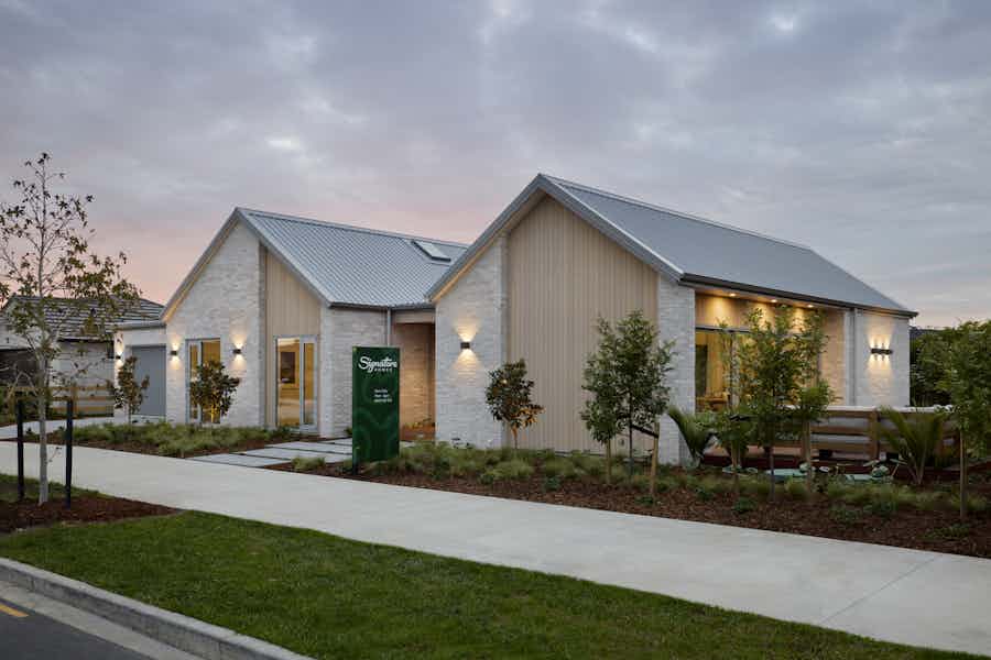 Signature Homes Clevedon showhome exterior at dusk with white-washed brick, timber cladding and steel roof, Auckland new home builder.