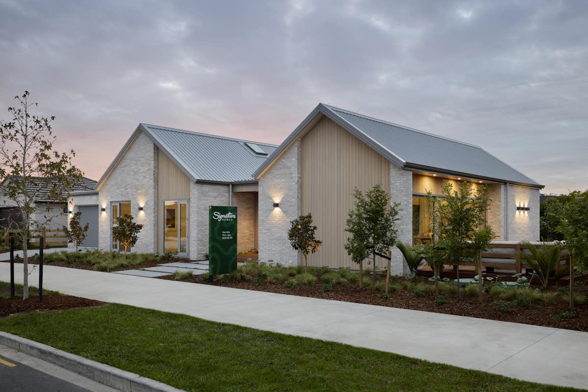 Signature Homes Clevedon showhome exterior at dusk with white-washed brick, timber cladding and steel roof, Auckland new home builder.