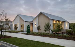 Signature Homes Clevedon showhome exterior at dusk with white-washed brick, timber cladding and steel roof, Auckland new home builder.