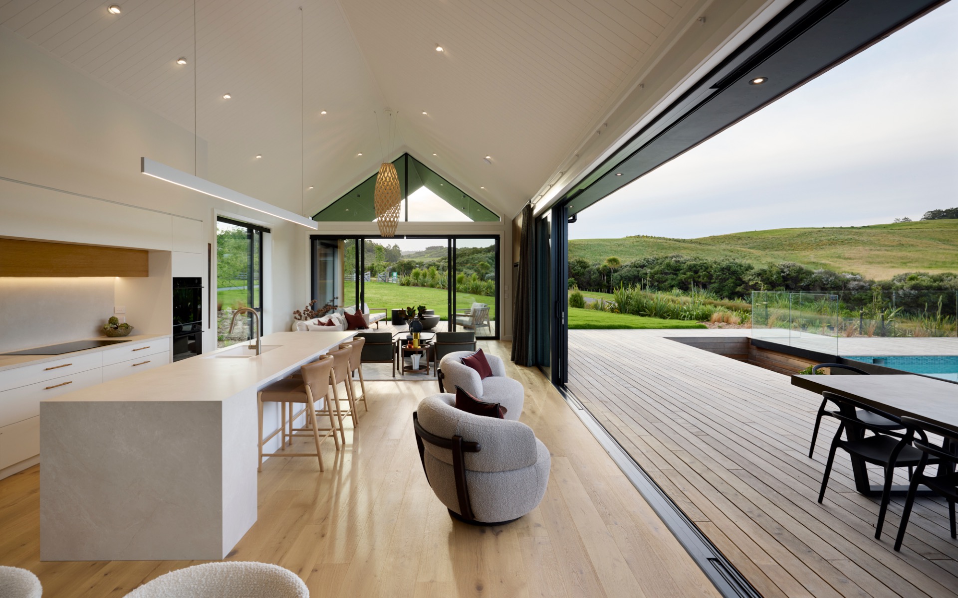 Open-plan kitchen and living area with vaulted ceiling and seamless indoor–outdoor flow to pool and decking.