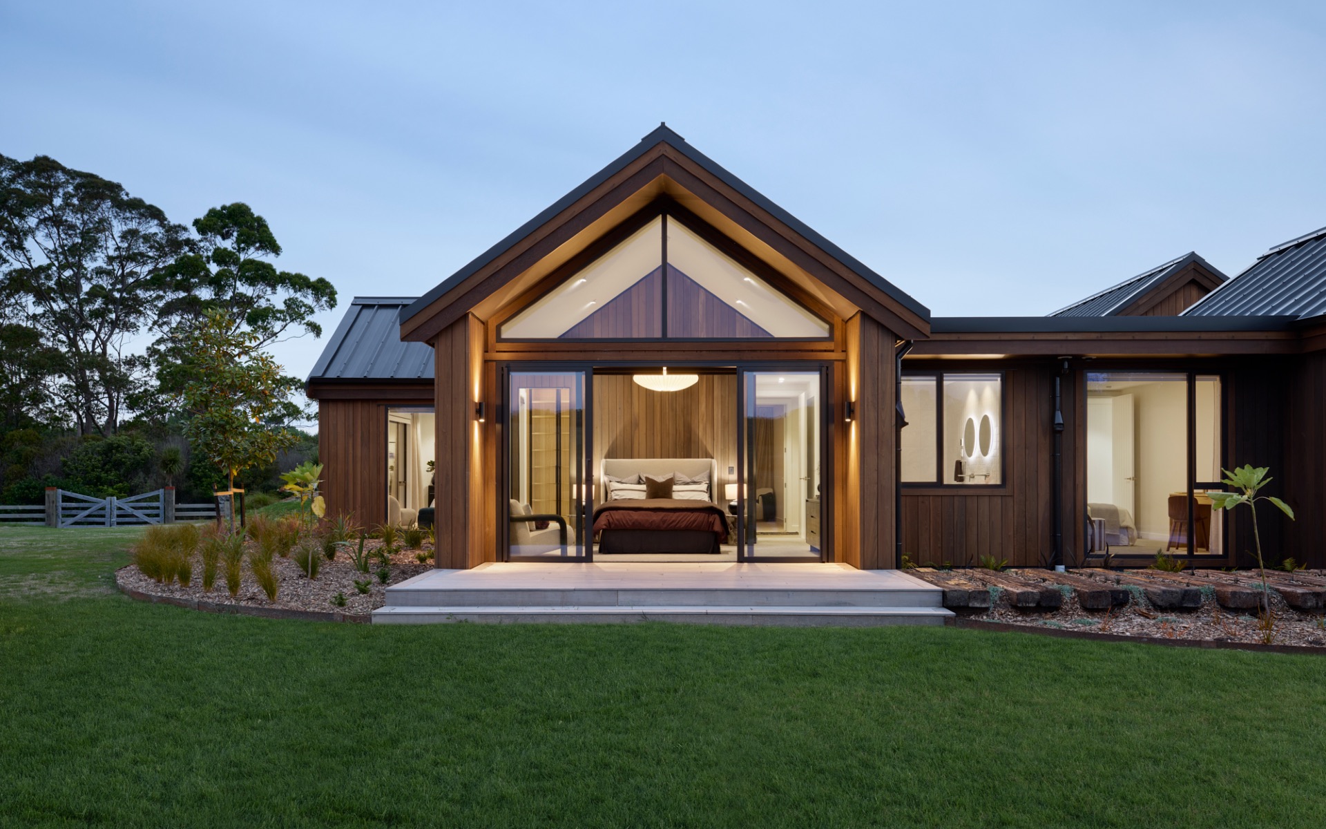 Master bedroom with gable ceiling, floor-to-ceiling windows, and cedar feature wall opening to landscaped gardens.