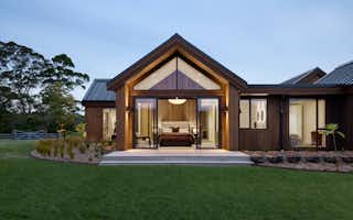Master bedroom with gable ceiling, floor-to-ceiling windows, and cedar feature wall opening to landscaped gardens.