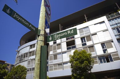 Modern apartment building with a telegraph pole in front with 2 street signs. One saying Joynton Avenue and one saying Epsom Road