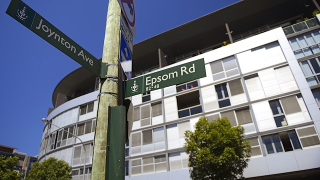Modern apartment building with a telegraph pole in front with 2 street signs. One saying Joynton Avenue and one saying Epsom Road
