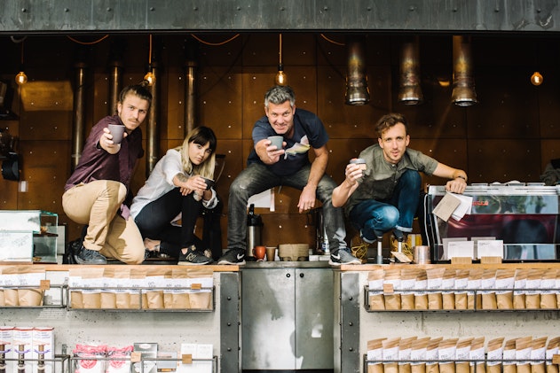 image of 3 men and one woman crouching on the counter of Single O cafe in Surry Hills holding out ceramic coffee cups