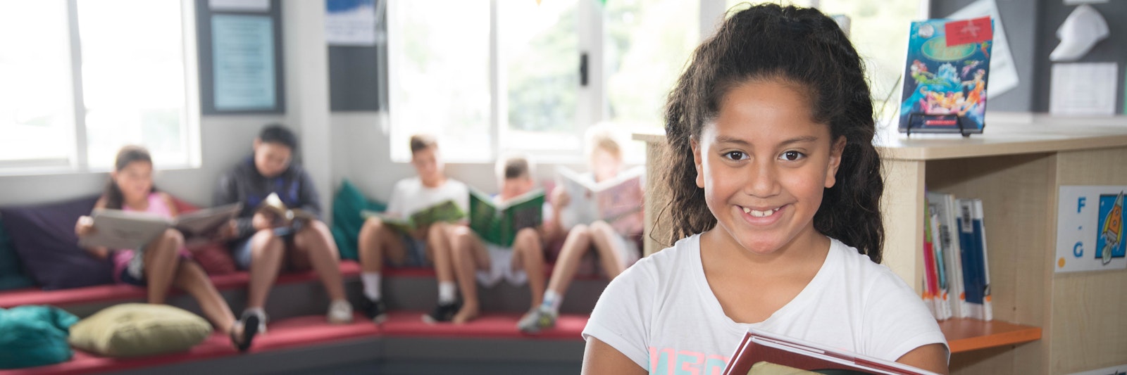 Girl stands in a library holding a book looking at the camera