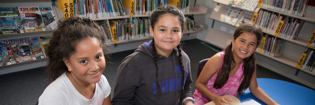 Three students sitting in a library, looking at the camera