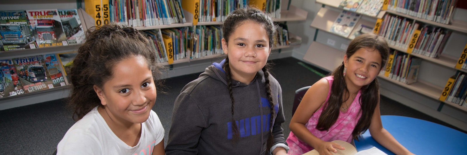 Three students sitting in a library, looking at the camera