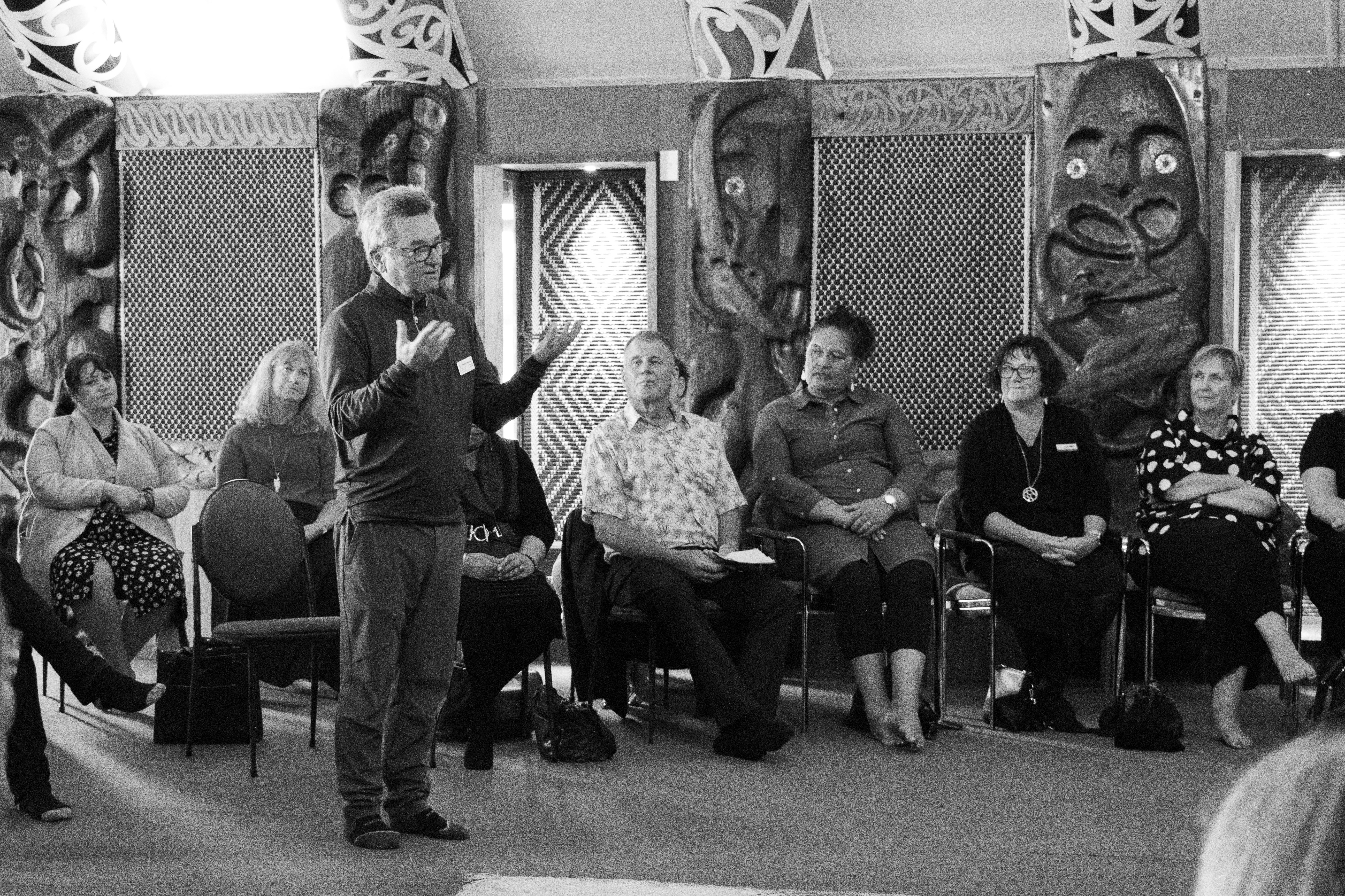 Person standing speaking to others inside a whare