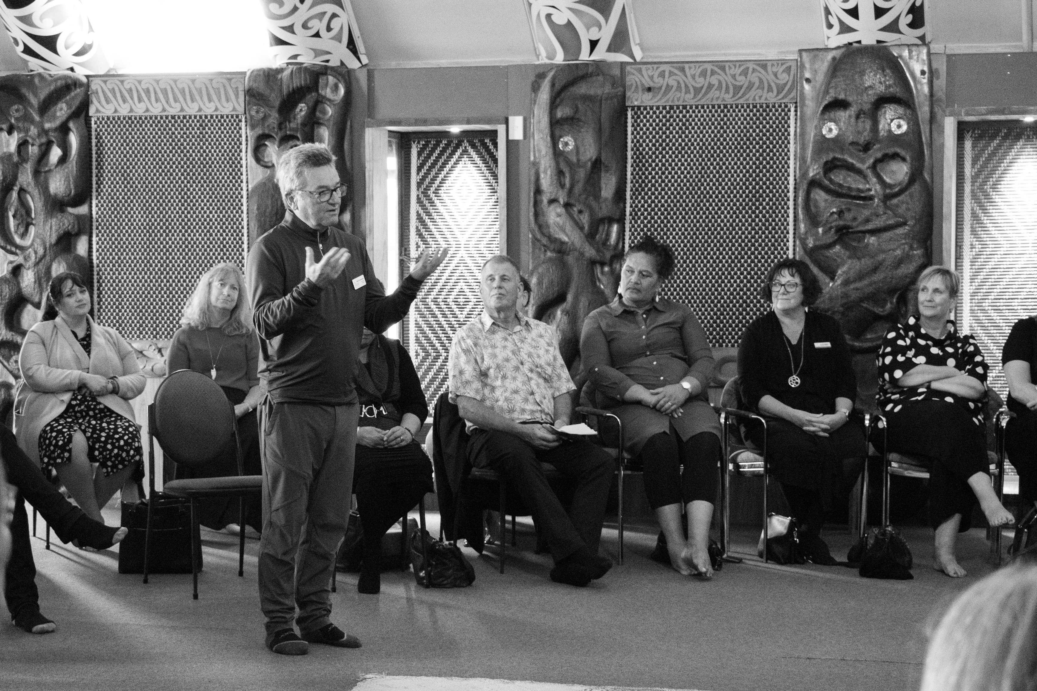 Person standing speaking to others inside a whare