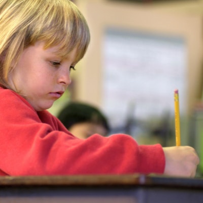 A child sits in a classroom, writing with a pencil