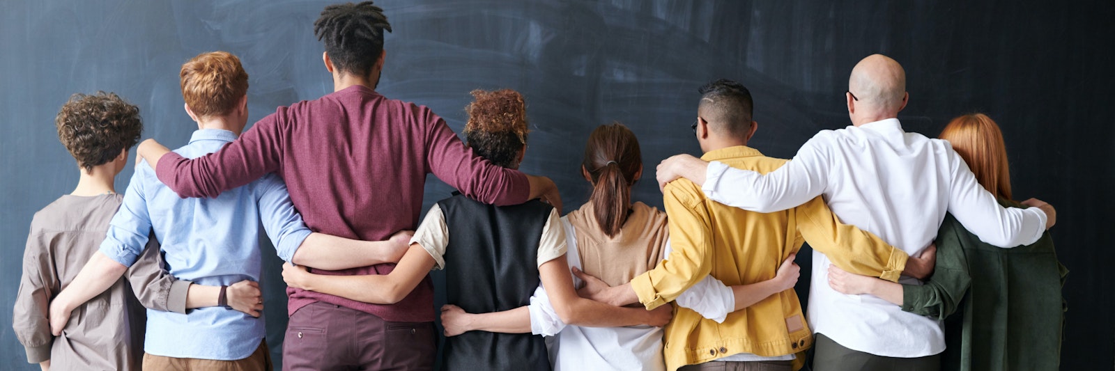 Group of adults standing with their arms around each other. The face away from the camera.