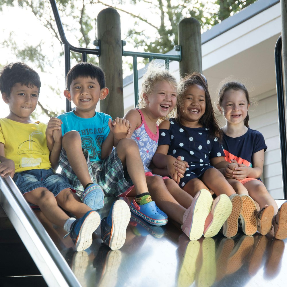 Five children sit at the top of a metal slide