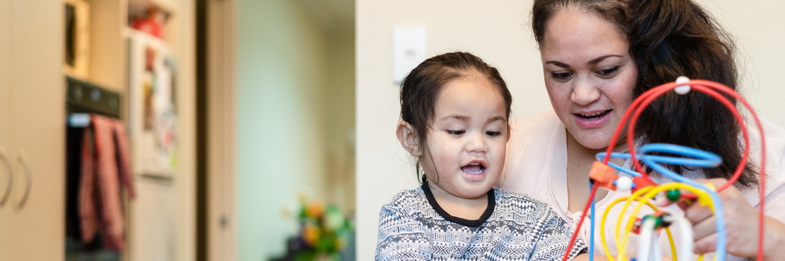 Woman sits on the floor with a pre-school childn. They are playing with an interactive toy