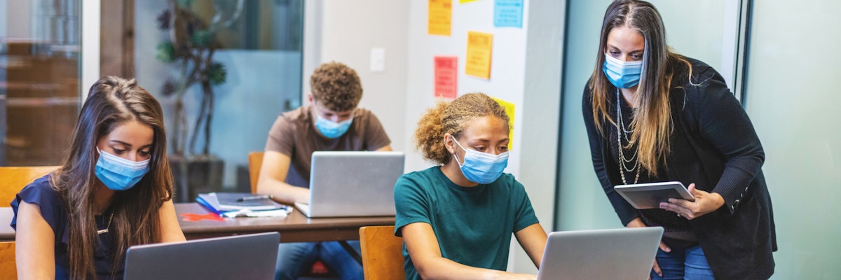 Students and a teacher in a classroom. They are all wearing face masks