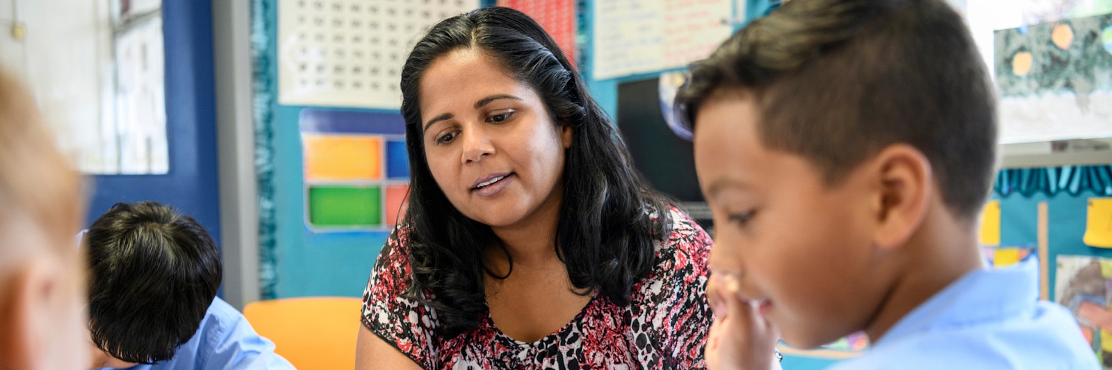 Teacher sits with a student in a classroom