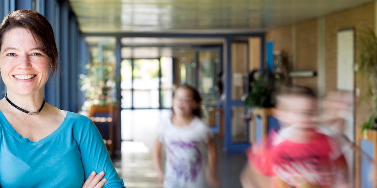 School leader smiling as she stands in a hallway while kids run past her.