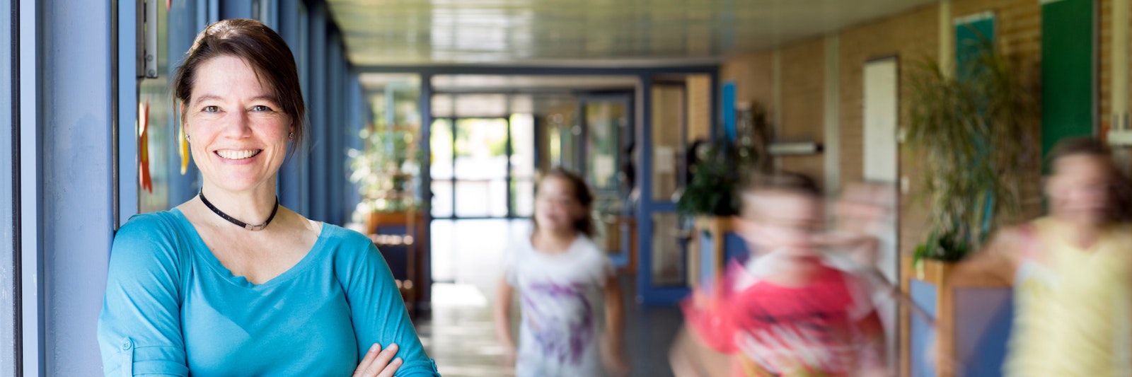 School leader smiling as she stands in a hallway while kids run past her.