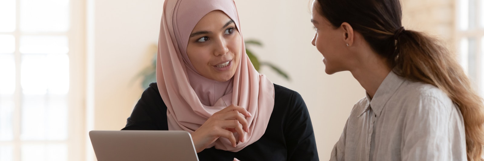woman with headscarf and laptop talking with colleague
