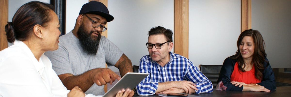 Group of adults sitting in a conference room looking at a tablet