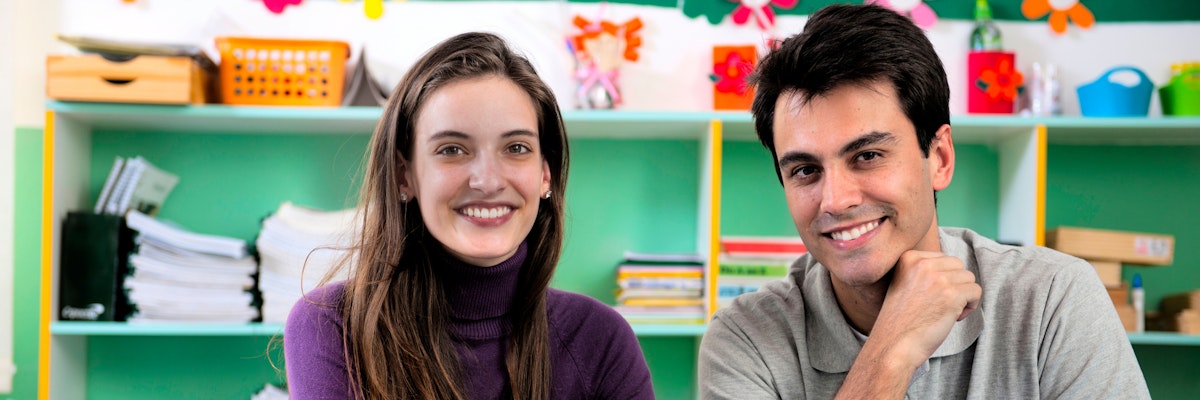 Two teachers sitting in a classroom, smiliing