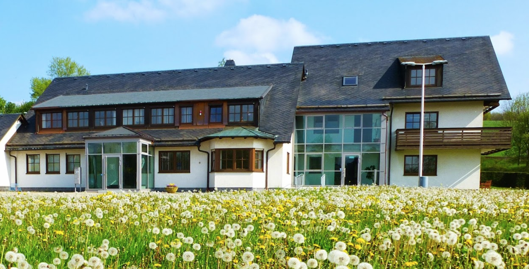 Blick auf das Gebäude der Stadtwerke Oelsnitz GmbH, davor eine Wiese mit Löwenzahn