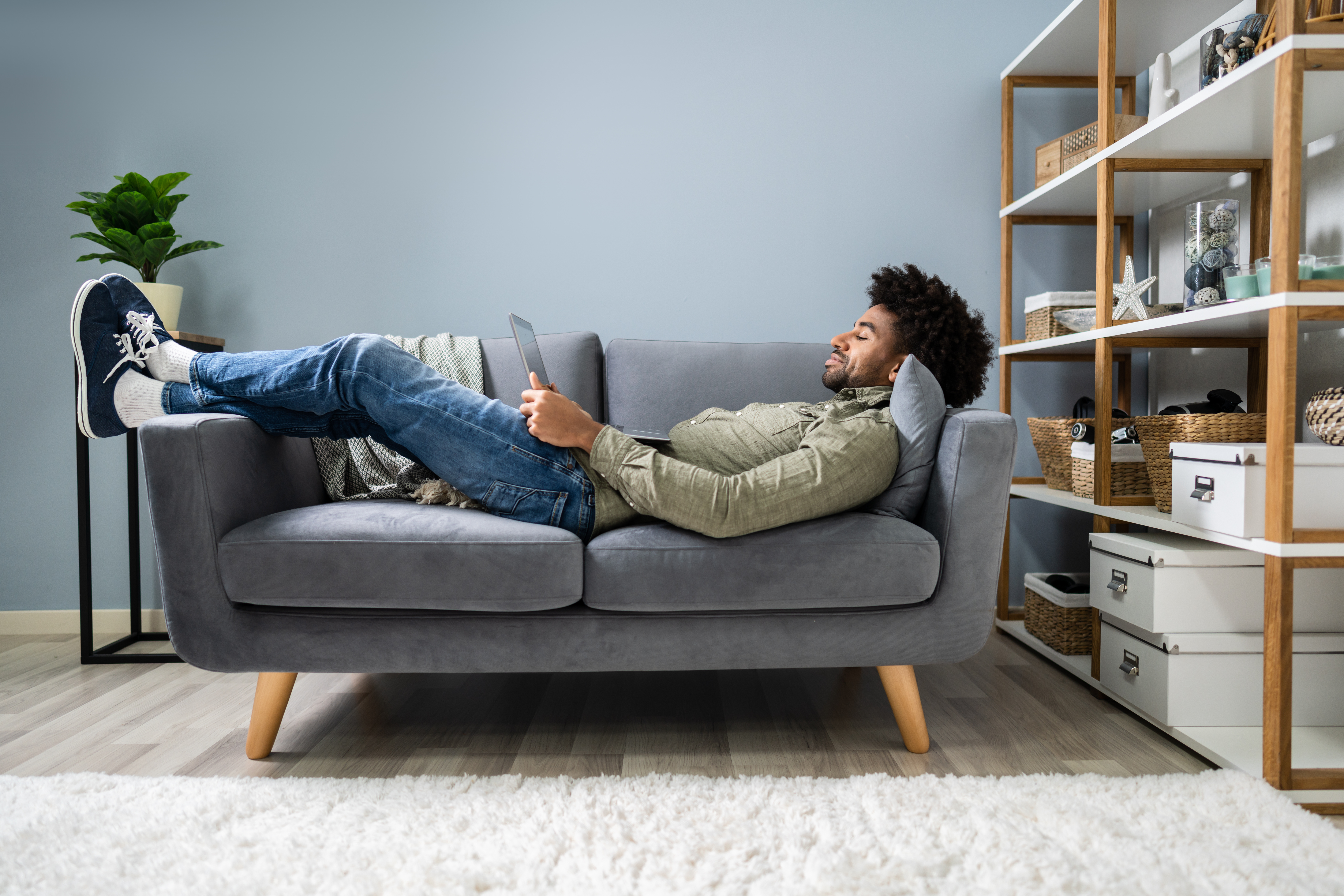 Mann liegt mit Laptop auf dem Schoß auf dem Sofa