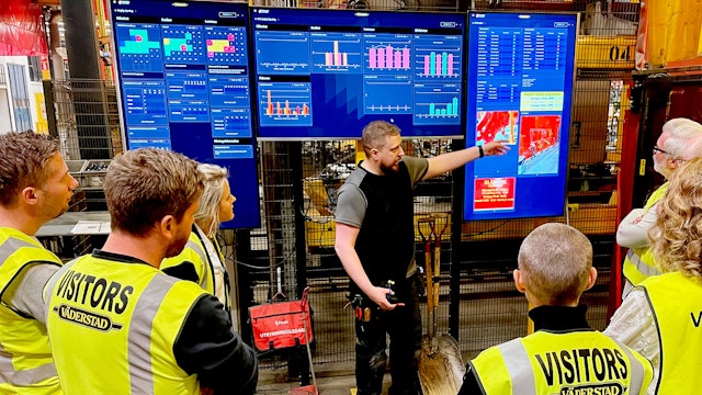 Medarbetare visar digitala Boards on Fire-tavlor för besökare i Väderstads produktionsmiljö.