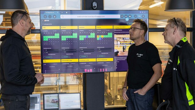 Three Svets & Smide employees standing by a Boards on Fire digital pulse board in a workshop environment.