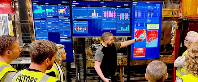 Grupp besökare följer en genomgång vid digitala styrningstavlor i Väderstads produktionsmiljö.